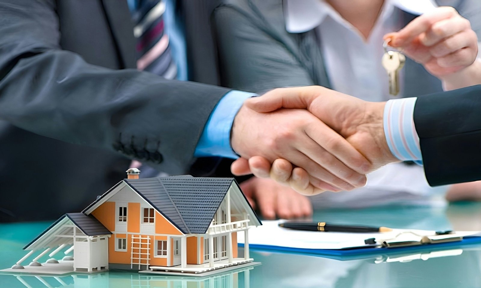 Home Two men shake hands over a table. A small model house and a set of keys sit on the table between them