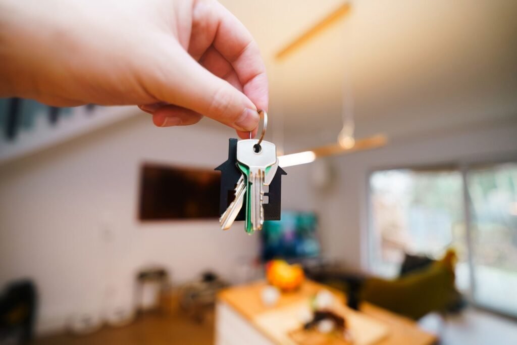 Contact A hand holds keys with a house keychain inside a modern, well-lit living space.